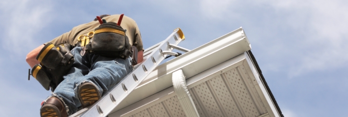 Contractor up a ladder repairing a roof showing uPVC cladding and blue sky